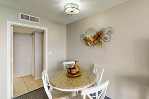 A dining area with a round wooden table, white chairs, and a decorative wall piece. - Bay Watch Resort 1615 (North Myrtle Beach)