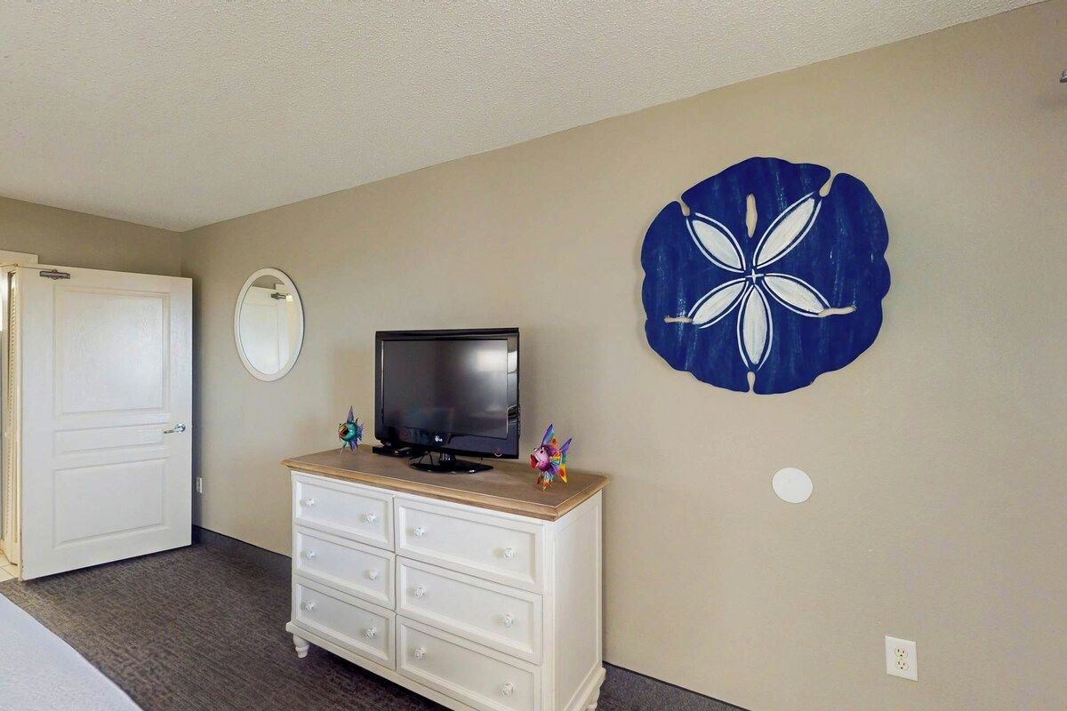 Una habitación con un aparador blanco, televisor, puerta y decoración en la pared.