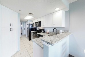 A modern kitchen with white cabinets, a granite countertop, and stainless steel appliances. - Bay Watch Resort 1614 (North Myrtle Beach)