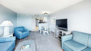 Ein modernes Wohnzimmer mit Flachbildfernseher, zwei Sofas, einem Couchtisch und einem Essbereich mit Stühlen.