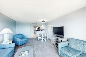 Ein modernes Wohnzimmer mit Flachbildfernseher, zwei Sofas, einem Couchtisch und einem Essbereich mit Stühlen.