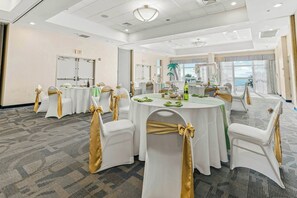 A conference room with round tables, white chairs, and gold sashes, equipped with ceiling lights and a view of the outdoors. - Bay Watch Resort 1619 (North Myrtle Beach)