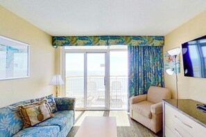 A room with a sofa, a chair, a desk, a TV, and a balcony with a view. - Bay Watch Resort 1702 (North Myrtle Beach)