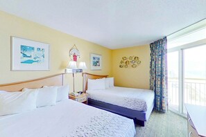 A hotel room with two beds, a nightstand, a lamp, and a window with curtains. - Bay Watch Resort 1702 (North Myrtle Beach)