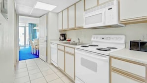 Cocina con electrodomésticos blancos, piso azul y vista a un comedor.