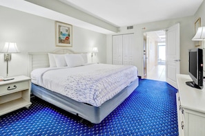 A hotel room with a bed, bedside lamps, a television, and a door leading to another room. - Bay Watch Resort 1717 (North Myrtle Beach)
