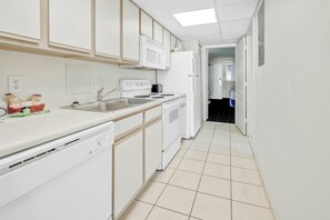 A narrow kitchen with white appliances, a dishwasher, and a sink. - Bay Watch Resort 1717 (North Myrtle Beach)