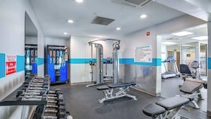 Un gimnasio con máquinas de pesas, bancos y un espejo grande.