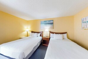 A hotel room with two beds, a nightstand with a lamp, a painting on the wall, and a window. - Bay Watch Resort 1710 (North Myrtle Beach)