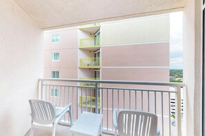 A balcony with two white chairs and a small table, overlooking a building with multiple balconies. - Bay Watch Resort 1710 (North Myrtle Beach)