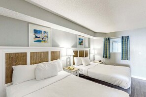 Ein Hotelzimmer mit zwei Betten, einem Nachttisch, einer Lampe und gerahmten Bildern an der Wand.