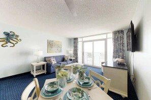 Hotelkamer met een eettafel voor vier personen, een bank, een televisie en een groot raam.