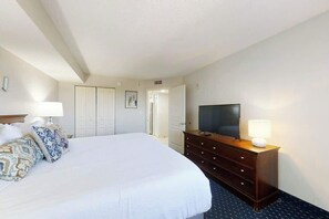 Een hotelkamer met een bed, een televisie, een dressoir en een deur die naar een andere kamer leidt.