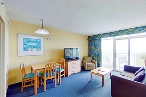 A room with a dining table, chairs, a television, a sofa, and a large window with a view. - Bay Watch Resort 1804 (North Myrtle Beach)