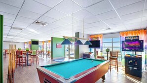 Une table de billard dans une pièce bien éclairée, avec un mur vert, un téléviseur et un appareil à sous.