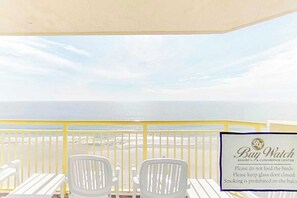 Ein Balkon mit weißen Stühlen und einem Tisch, mit Blick auf einen Strand. Ein Schild weist darauf hin, dass das Füttern von Vögeln verboten, Fenster und Türen geschlossen und Rauchen auf dem Balkon untersagt ist.