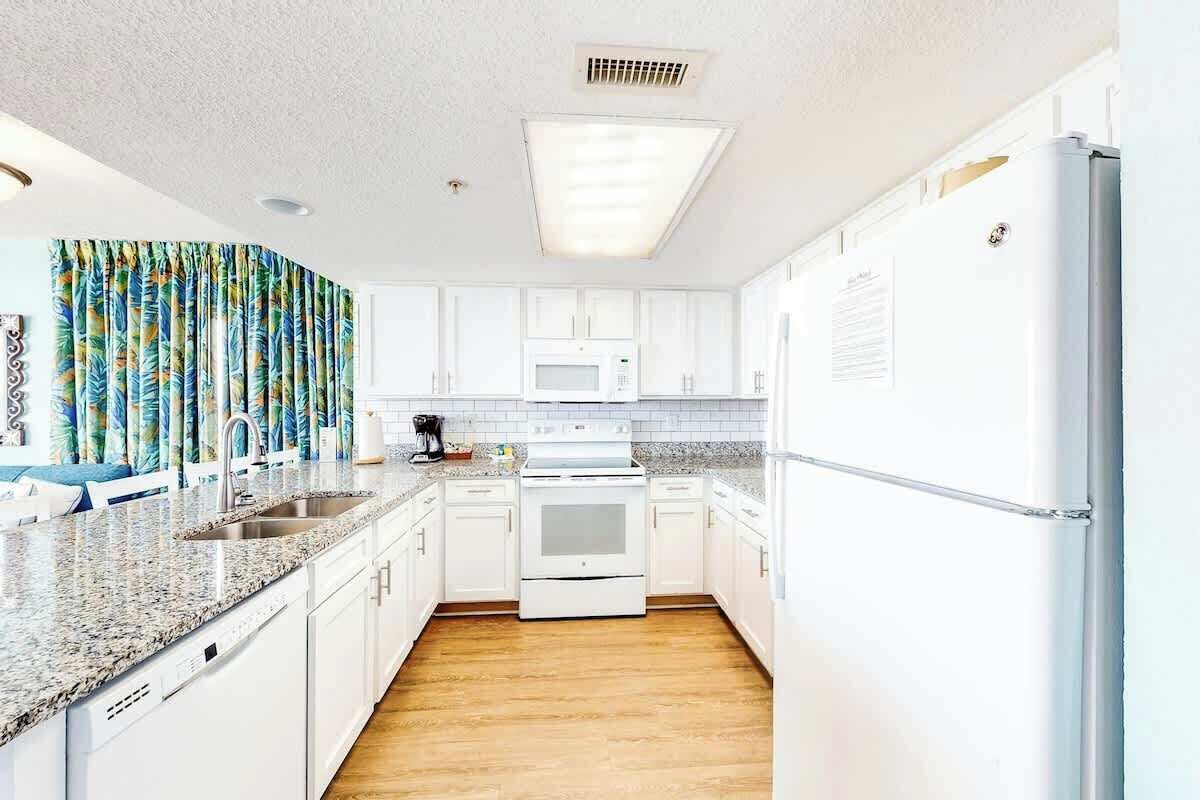 A kitchen with white cabinets, a granite countertop, a built-in microwave, and a stainless steel refrigerator.