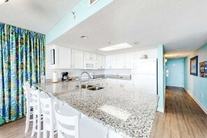 A modern kitchen with white cabinets, a granite countertop, and a stainless steel sink. - Bay Watch Resort 1809 (North Myrtle Beach)