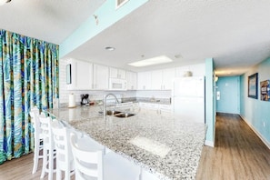 A modern kitchen with white cabinets, a granite countertop, and a stainless steel sink. - Bay Watch Resort 1809 (North Myrtle Beach)