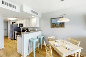 Une cuisine moderne avec des meubles blancs, un îlot central doté de tabourets et un coin repas avec une table dressée pour quatre personnes.