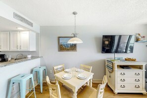 Un coin repas avec une table dressée pour quatre personnes, un téléviseur fixé au mur et un meuble avec des tiroirs.