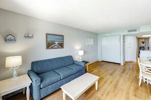 A living room with a blue sofa, a white coffee table, and a painting on the wall. - Bay Watch Resort 1820 (North Myrtle Beach)