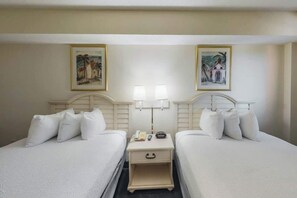 Ein Hotelzimmer mit zwei Betten, Nachttischen, Lampen und gerahmten Kunstwerken an den Wänden.