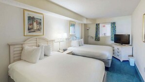 Ein Hotelzimmer mit zwei Betten, einem Fernseher, einem Schreibtisch mit Lampe und einem Bild an der Wand.