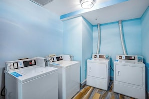 A laundry room with four white washing machines and dryers, a control panel, and ventilation ducts. - Bay Watch Resort 1906 (North Myrtle Beach)