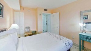 A hotel room with a bed, a chair, a desk, and a door leading to another room. - Bay Watch Resort 1906 (North Myrtle Beach)