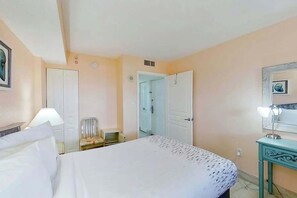 A hotel room with a bed, a chair, a desk, and a door leading to another room. - Bay Watch Resort 1906 (North Myrtle Beach)