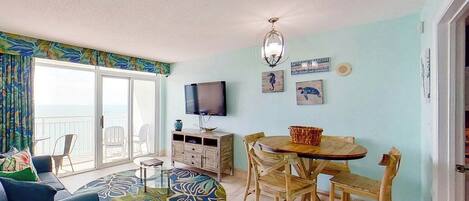 A room with a dining table, chairs, a television, and artwork on the wall.
