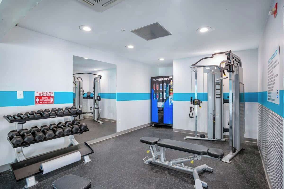 A gym with weightlifting equipment, benches, and a mirrored wall.