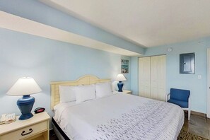A hotel room with a bed, two bedside lamps, a chair, a wardrobe, and a small table with a lamp. - Bay Watch Resort 1919 (North Myrtle Beach)