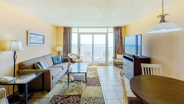 Un salon avec un canapé, une table basse, un téléviseur et un balcon offrant une vue agréable.
