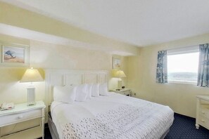 A hotel room with a large bed, two bedside tables with lamps, a window with curtains, and artwork on the walls. - Bay Watch Resort 1920 (North Myrtle Beach)