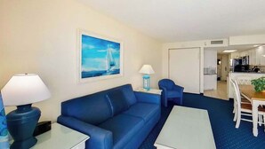 A living room with a blue sofa, a coffee table, a lamp, and a painting of a sailboat on the wall. - Bay Watch Resort 1920 (North Myrtle Beach)