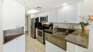 A kitchen with white cabinets, a granite countertop, a stainless steel refrigerator, a microwave, an oven, and a sink. - Bay Watch Resort 1920 (North Myrtle Beach)