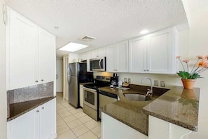 A kitchen with white cabinets, a granite countertop, a stainless steel refrigerator, a microwave, an oven, and a sink. - Bay Watch Resort 1920 (North Myrtle Beach)