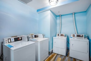 A laundry room with four white washing machines, two dryers, and a blue wall. - Bay Watch Resort 1920 (North Myrtle Beach)