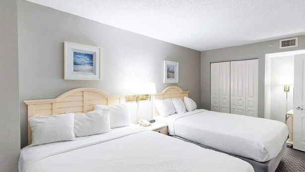 A hotel room with two beds, a wardrobe, and a nightstand with a lamp. - Bay Watch Resort 1921 (North Myrtle Beach)
