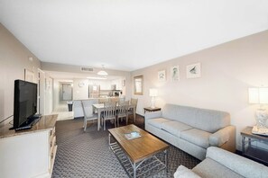 A living room with a sofa, coffee table, TV, and a dining area with chairs and a table. - Bay Watch Resort 1921 (North Myrtle Beach)
