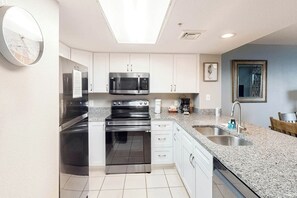 A modern kitchen with stainless steel appliances, white cabinets, a granite countertop, and a skylight. - Bay Watch Resort 1921 (North Myrtle Beach)