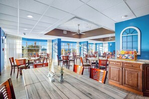 A restaurant with multiple tables and chairs, a ceiling fan, and a view of the outdoors. - Bay Watch Resort 1934 Oceanfront (North Myrtle Beach)