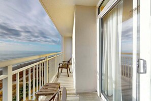 A balcony with a view of the beach, a wooden table, and a chair. - Camelot by the Sea 0809 (Myrtle Beach)