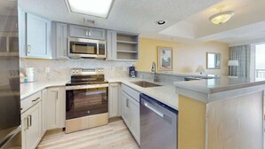 A modern kitchen with built-in appliances, a dishwasher, and a large island. - Camelot by the Sea 0809 (Myrtle Beach)