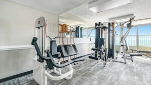 A gym with exercise equipment, a mirror, and a view of the outdoors. - Camelot by the Sea 0809 (Myrtle Beach)