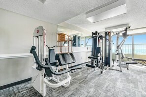 A gym with exercise equipment, a mirror, and a view of the outdoors. - Camelot by the Sea 0809 (Myrtle Beach)