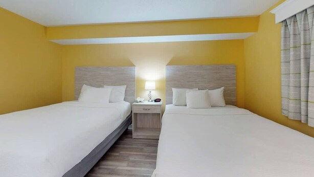 A hotel room with two beds, a nightstand with a lamp, and a window with curtains. - Camelot by the Sea 0809 (Myrtle Beach)