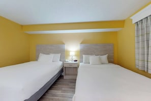 A hotel room with two beds, a nightstand with a lamp, and a window with curtains. - Camelot by the Sea 0809 (Myrtle Beach)